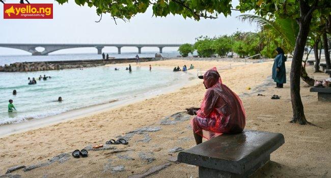 A man sits under a tree as it rains at Artificial Beach in Malé on May 15, 2026