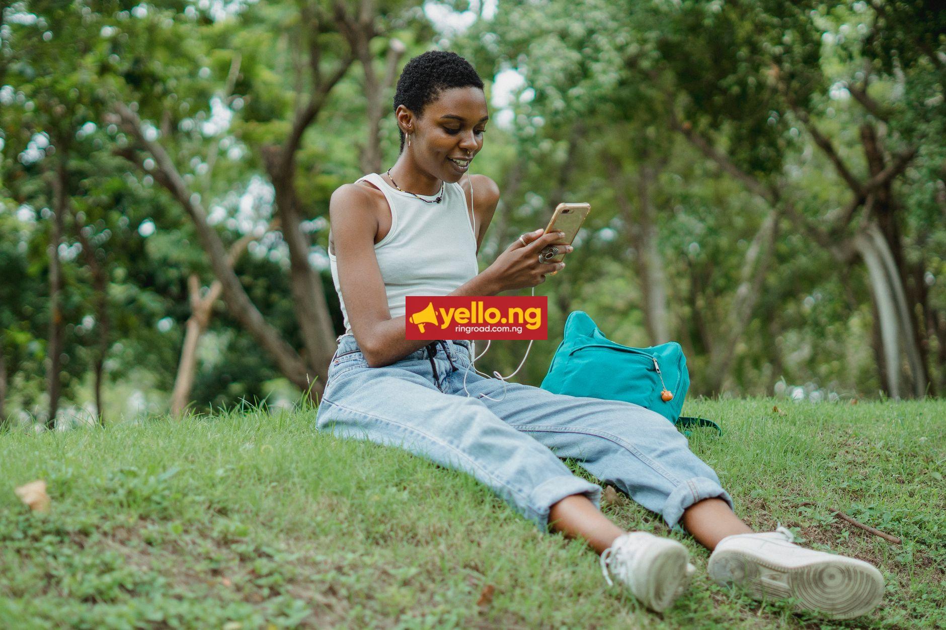 Young African woman smiling while listening to Afrobeats music on her smartphone with earphones outdoors