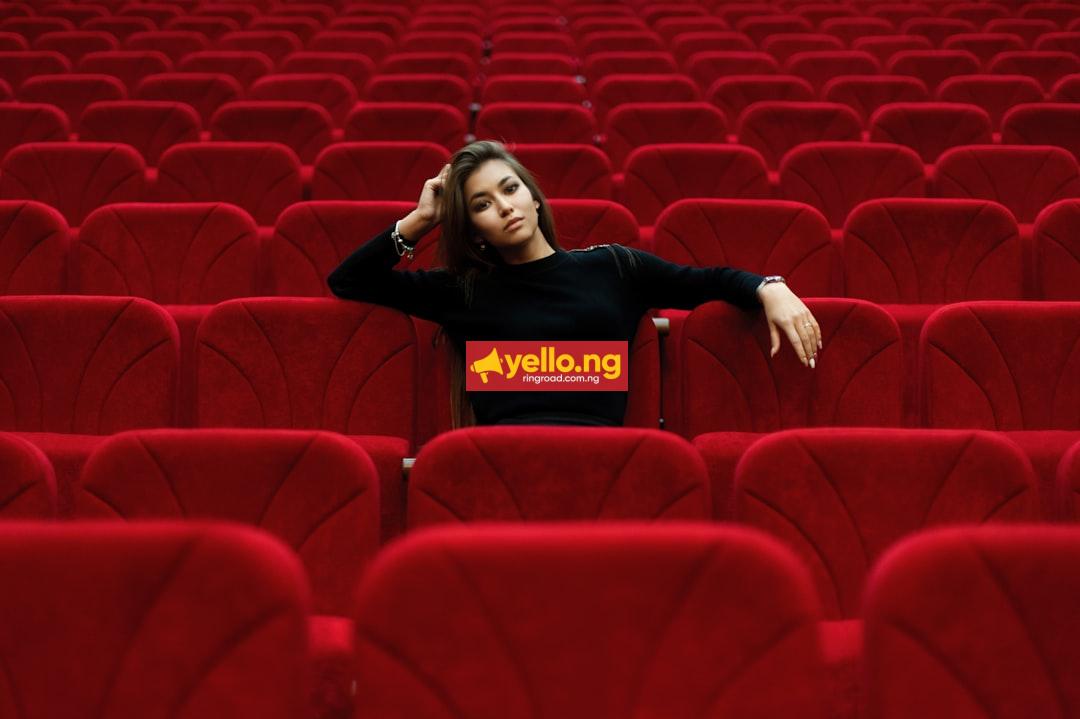 A lone woman sitting in an empty red cinema theater, evoking solitude and the world of film